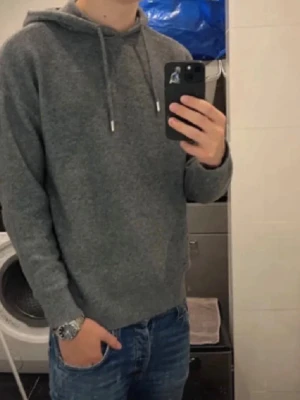 Grå ull hoodie från Zara - Säljer en stilren grå hoodie från Zara med huva och dragsnören. Hoodien har en mjuk och skön känsla, perfekt för chill dagar. Långa ärmar och enkel design utan tryck eller logga framtill. Passar till jeans eller joggers för en avslappnad look.