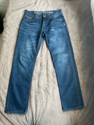 Jeans från Armani Exchange (nypris 1000+) - Snygga blå jeans från Armani Exchange med raka ben och klassisk femficksmodell. Jeansen har tydliga slitningar framtill och vit logga på insidan av linningen. Tillverkade i denim med kontrastsömmar för en cool look. Där finns en liten fläck som syns på sista bilden, går kanske bort i tvätten, har ej testat🥰 Nypris 1000+