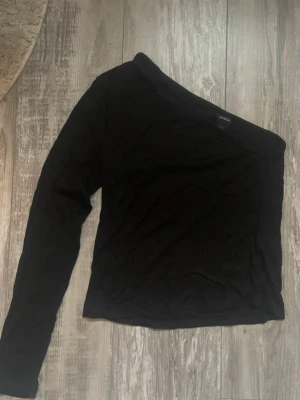 Svart oneshoulder topp från Lindex - Säljer en svart oneshoulder topp från Lindex i mjukt material. Toppen har lång ärm på ena sidan och är axelbandslös på andra. Storlek S!