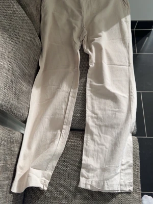 Beiga linnebyxor med raka ben - Snygga beiga linnebyxor med raka ben och avslappnad passform. Byxorna har fickor både fram och bak och är tillverkade i ett lätt och luftigt linnematerial. Perfekta för en chill och stilren look.
