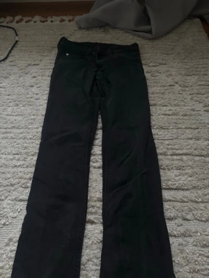 Svarta bootcut jeans - Säljer ett par svarta bootcut jeans med klassisk femficksdesign och knappgylf. Jeansen har en rak passform över låren och lätt utsvängda ben. Perfekta för dig som gillar en tidlös och enkel stil.