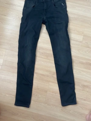 Svarta jeans från Replay - Säljer ett par svarta  jeans från Replay med klassisk femficksdesign och diskret logga på myntfickan. Jeansen har smal passform och är tillverkade i stretchigt denimtyg för extra komfort. Perfekta för en trendig och avslappnad look.