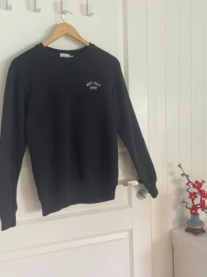 Svart sweatshirt från KappAhl - Svart sweatshirt från KappAhl med trycket 'West Coast 1978' på bröstet. Klassisk rund halsringning och ribbade muddar vid ärmslut och nederkant. Perfekt för en avslappnad och stilren look.