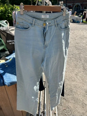 Ljusblå jeans från Lindex - Säljer ett par ljusblå jeans från Lindex med klassisk femficksmodell och hög midja. Jeansen har raka ben och rå kant nedtill för en trendig look. Tillverkade i mjuk denim med dragkedja och knapp framtill.
