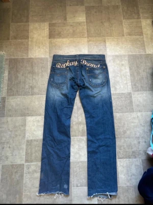 Vintage blå bootcut replay jeans med embroidery 2000s low rise - Säljer ett par blå jeans från Replay Brand med broderad logga över bakfickorna. Jeansen har lite utsvängda ben slitna detaljer och fransade benslut. Nice fade på och på och dem är low rise W30 L32 