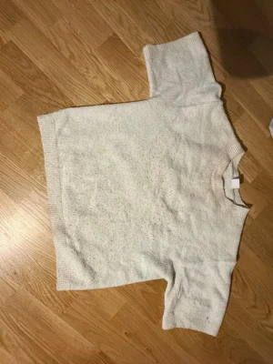 Vit oversize stickad tröja - Mysig vit stickad tröja i oversize-modell med korta ärmar och ribbade kanter. Tröjan har en enkel, stilren design och är perfekt för lager-på-lager. Passar dig som gillar en avslappnad och trendig look.
