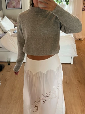 Grå stickad  - Mysig  stickad tröja i ljusgrått med hög hals och långa ärmar. Tröjan har en avslappnad passform och ribbstickade muddar vid ärmslut och hals. Perfekt att styla med kjol eller jeans för en chill look.