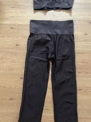Bruna  leggings med hög midja + topp från DOM - Säljer ett par bruna  leggings från DOM med bred, hög midja för extra komfort. De är långa och har en slimmad passform som sitter snyggt på benen. Perfekta för träning eller chill. Materialet är stretchigt och följsamt.