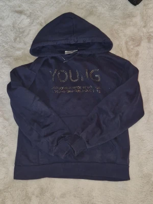 Mörkblå hoodie, gina tricot - Snygg mörkblå hoodie med huva och texten 'YOUNG' framtill i glittrande strass. Texten fram har tappat några diamanter och ena snöret har sprättat upp sig lite men annars är den helt ok! Pris på den kan diskuteras💕 