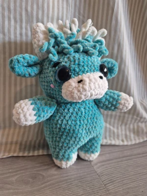 Blå virkad kossa mjukisdjur - Supergullig handvirkad kossa i blått och vitt plyschgarn med stora svarta ögon och små rosa kinder. Den har lockig man, svans och mjuka öron. Perfekt som dekoration eller present till någon som gillar söta gosedjur.