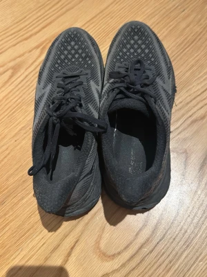 Svarta Hoka sneakers med mönster - Säljer ett par svarta sneakers från Hoka med snyggt geometriskt mönster på ovandelen. Skorna har tjock sula för extra komfort och Hoka-logga på sidan. Ovandelen är i meshmaterial som andas och de har klassisk snörning.