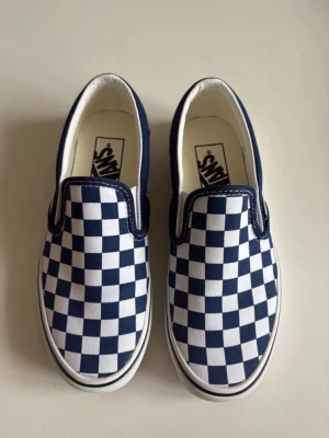 Vans blåvita slip-ons - Klassiska Vans slip-on sneakers med blåvitt checkerboard-mönster. Endast använda en gång, som nya. Storlek 36! :)