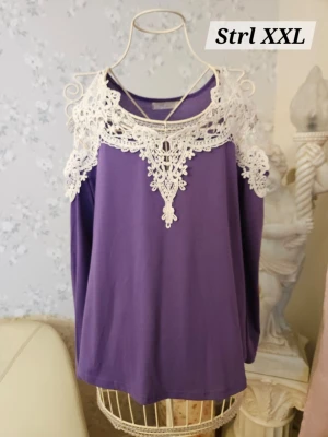 Lila topp med spetsdetaljer - Säljer en lila topp med vackra vita spetsdetaljer runt halsringningen och axlarna. Toppen har off-shoulder design och ett elegant fall. 