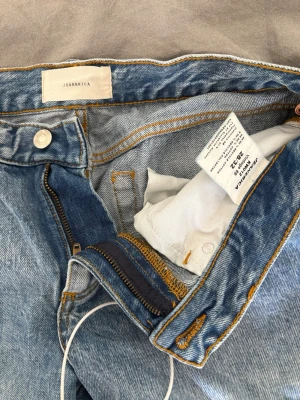 Blå Kyoto jeans från Jeanerica - Säljer ett par ljusblå jeans från Jeanerica med utsvängda ben och klassisk femficksmodell. Jeansen har dragkedjegylf, kontrastsömmar och är tillverkade i 100% bomull. I färgen vintage 69. W28L32