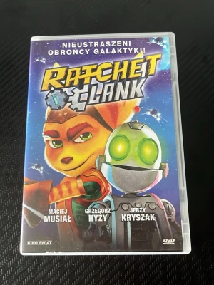 Ratchet & Clank DVD-film - Säljer en DVD-film med Ratchet & Clank, baserad på det populära spelet. Omslaget är färgglatt med karaktärerna Ratchet och Clank i fokus mot en rymdinspirerad bakgrund. Filmen är på polska och kommer i ett plastfodral. Perfekt för dig som gillar animerade äventyr och sci-fi.