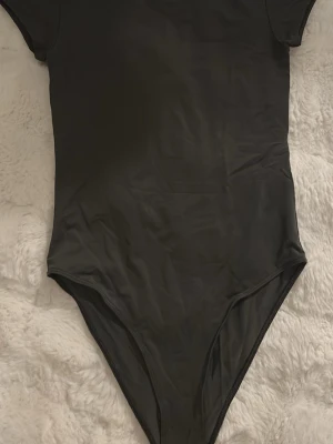 Mörkgrå kortärmad body - En enkel och stilren Mörkgrå body med korta ärmar och rund hals. Tillverkad i ett mjukt material som sitter tight mot kroppen. Perfekt att styla med jeans eller kjol för en clean look.