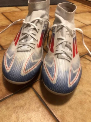 Adidas F50 - Säljer ett par lätta och bekväma fotbollsskor med modern design i vitt, rött och blått. Perfekta för dig som vill ha kvalitet till ett bättre pris