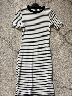 Randig klänning med svart krage - Snygg kortärmad klänning med svarta och vita horisontella ränder och svart krage. Modellen är figurnära och har en klassisk t-shirtform upptill. Perfekt för dig som gillar enkel och stilren design.