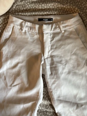 Beiga chinos från BikBok - Snygga beiga chinos/kostymbyxor från BikBok i storlek 34. Klassisk utsvängd passform med fickor fram och en dekorativ bakficka. Byxorna har hällor för skärp och stängs med dragkedja och knapp. Perfekta för en clean och stilren look. De är också med slits dere på benen!💘