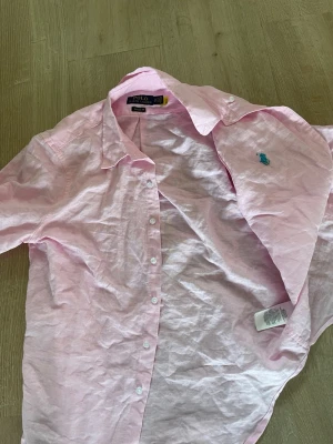 Rosa linne skjorta - Säljer en klassisk ljusrosa linne skjorta från Polo Ralph Lauren med turkost broderat logomärke på bröstet. Storlek S. Väldigt bra skick. 