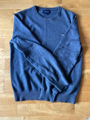 Blå tröja från Lexington - Snygg blå tröja från Lexington med rund halsringning och diskret logotyp på bröstet. Tröjan har långa ärmar och ribbade muddar vid ärmslut och nederkant. Perfekt för dig som gillar stilrena plagg med enkel design.Nästan helt ny