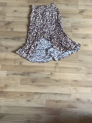 Leopardmönstrad långkjol - Säljer en flowy långkjol med leopardmönster i beige, brunt och svart. Kjolen har en lätt volangkant och är tillverkad i ett mjukt, tunt material som ger ett snyggt fall. Perfekt för dig som vill sticka ut med ett djurmönster.