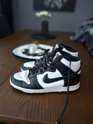 Nike Dunk High Panda sneakers - Nike Dunk High sneakers i svart och vitt läder med klassisk Swoosh på sidan. Högt skaft, svart snörning och perforerad tåbox för extra ventilation. Stilren och tidlös modell som passar till många olika outfits.