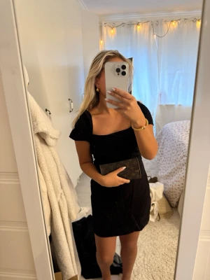 Zara Svart söt klänning med fyrkantig ringning - Snygg svart kort klänning med fyrkantig ringning och korta ärmar. Klänningen har en enkel och stilren design som passar perfekt till accessoarer. Materialet ser ut att vara mjukt och följsamt, vilket ger en bekväm passform.