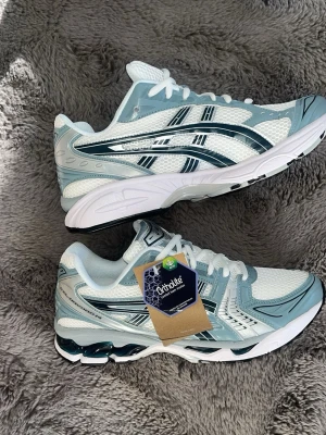 ASICS vita och ljusblå sneakers - Snygga sneakers från ASICS i vitt och ljusblått med klassiska svarta detaljer på sidorna. Ovandelen är i mesh och syntet för bra andningsförmåga och komfort. Skorna har Ortholite-innersula och en chunky sula med svart mönster undertill.