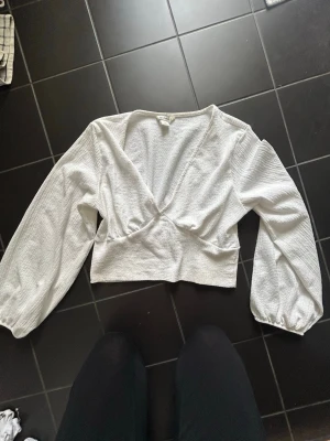 Vit topp med v-ringning - Säljer en vit topp med v-ringning och långa ärmar. Toppen är croppad och perfekt för dig som gillar stilrena och trendiga plagg. Jag fick två stycken när jag fyllde år så den är aldrig använd men prislappen är borttagen. 