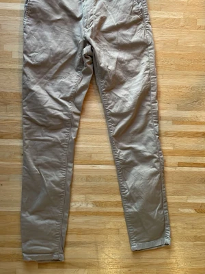 Beige chinos från These Glory Days - Snygga beige chinos från These Glory Days med klassisk rak passform. Tillverkade i mjukt bomullstyg som känns skönt mot huden. Perfekta för en clean och stilren look. Skandinavisk design med diskreta detaljer och fickor både fram och bak.