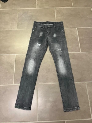 Grå slitna Dsqcdabd2 jeans - Säljer ett par grå slim fit jeans med slitningar och blekta detaljer. Jeansen har klassisk femficksdesign och knappstängning. Materialet är denim och passformen är smal. Perfekt för dig som gillar en cool och avslappnad stil.