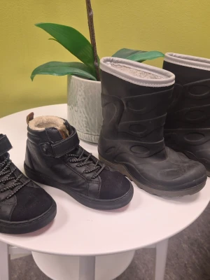 Exani gummistövlar, Lejon kängor svarta storlek 28 - Två par svarta boots, ena paret är höga vinterstövlar med mönstrad yta och ljus foder, andra paret är stövletter med snörning, kardborre och mjukt foder. Perfekta för kalla dagar och håller fötterna varma.