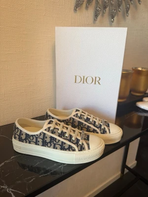 Dior Oblique sneakers i blått och vitt - Snygga Dior Oblique sneakers med blått och vitt mönster, klassisk låg modell med rund tå och vit gummisula. Skorna har 'Christian Dior' på tungan och är tillverkade i canvas med detaljer i läder. Perfekt för dig som vill ha en exklusiv och trendig look. Äkthetsbevis följs med såklart