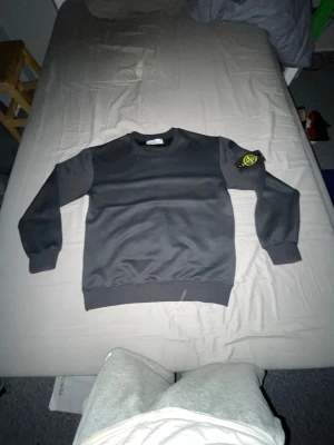 Svart sweatshirt från Stone Island - Svart sweatshirt från Stone Island med klassisk rund hals och ribbade muddar. Ikonisk Stone Island patch sitter på vänster ärm. Tröjan har en clean och stilren design, perfekt för dig som gillar streetwear och exklusiva märken.