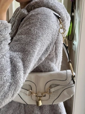 Y2k vit axelväska med hänglås och gulddetaljer  - Snygg vit axelväska i croco-mönstrat konstläder med guldfärgade metalldetaljer😍Väskan har en unik design med svarta kanter och dekorativt hänglås framtill. Axelremmen är en mix av kedja/cirklar och läder, vilket ger en cool kontrast! Supercool väska som ökar snyggheten på din outfit💗Den är rymlig inuti till accessoarer och mobiltelefon! Stängs med en metallmagnet. Använd några gånger, inga stora defekter🤍Hör av vid frågor, pris diskuterbart❤️