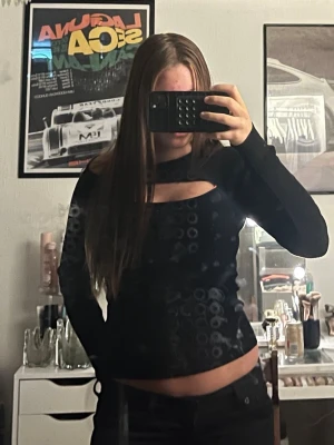 Svart långärmad topp med cut out - Snygg svart långärmad topp med unik cut out-detalj över bröstet. Toppen har en tight passform och är croppad så den visar lite av magen. Perfekt för dig som vill ha en trendig och stilren look.
