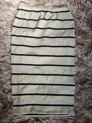 Beige och blå randig långkjol - Säljer en beige långkjol med mörkblåa horisontella ränder. Kjolen har en rak passform och är gjord i ett mjukt, frottéliknande material. Perfekt för dig som gillar en avslappnad men ändå stilren look.