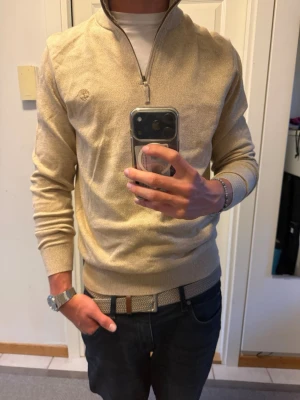 Beige stickad tröja Timberland - Snygg beige stickad tröja från Timberland med halv dragkedja och diskret logga på bröstet. Tröjan har ribbade muddar och krage, perfekt för lager på lager. Tillverkad i mjukt material som känns skönt mot huden. Splitter ny med tags