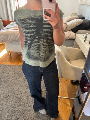 Grå t-shirt med tryck - Grå t-shirt med svart skelettmönster på framsidan. T-shirten har rund hals och har korta ärmar. Perfekt för dig som gillar edgy och unika prints💗💗