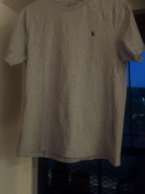 Grå Ralph lauren t-shirt med liten logga - En enkel grå t-shirt i bomull med korta ärmar och rund hals. På bröstet finns en liten broderad logga i mörk färg. Perfekt till jeans eller shorts för en clean och stilren look.