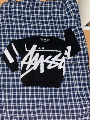 Stüssy tröja - Som ny! Säljer en svart tröja från Stüssy med stor vit logga över hela framsidan och baksidan. Tröjan har långa ärmar med vita ränder på ena ärmen och är i en normal passform. Perfekt för dig som gillar streetwear och vill sticka ut. Köpt på Sellpy! 