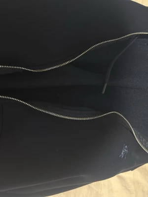 Svart hoodie med dragkedja - Svart hoodie med dragkedja framtill och huva med dragsko. Klassisk modell med fickor på sidorna och mjukt material, perfekt för en avslappnad stil.