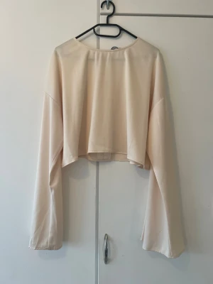Krämvit blus med vida ärmar -  Krämvit blus i ett tunt material. Med vida långärmar och rund halsringning. Även knappar längs ryggen som ger en extra detalj. Perfekt att styla med höga jeans eller kjol! Har använt några fåtal gånger. 