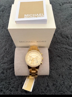 Guldig klocka från Michael Kors - Snygg guldig klocka från Michael Kors med länkarmband och glittrande stenar runt urtavlan. 