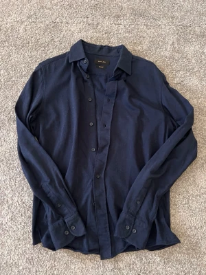 Mörkblå skjorta från Massimo Dutti - Snygg mörkblå skjorta från Massimo Dutti i mjukt jerseytyg. Klassisk krage, knäppning framtill och långa ärmar med manschettknappar. Perfekt till jeans eller chinos för en clean look.
