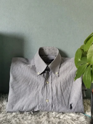  Randig Ralph Lauren skjorta  - POLO RALPH LAUREN SKJORTA Storlek : S Användning: Skjortan är i bra skick, dock har skjortan lite defekter, men inget som syns på mycket vid användning(se bild 5 och 6) Nypris: 1800SEK Modellen på bilden är 184 och väger 76KG Skickas inom 24h