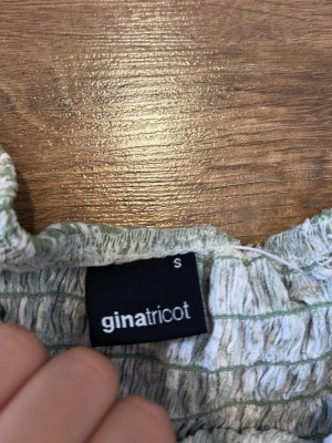 Grön blommig volangkjol Gina Tricot - Supersöt kortkjol från Gina Tricot i ljusgrönt med vitt blommönster. Kjolen har volangkant och smock i midjan för en bekväm och snygg passform. Perfekt för dig som gillar en feminin och trendig stil. Säljs ej längre på Gina inga defekter 