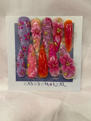 Fantasy (L);Extra Long Stiletto - Snygga handgjorda press-on naglar i en extra långa stilettoform med mix av lila, rosa och orange. Dekorerade med handgjord 3D-blommor, guldiga detaljer och små pärlor. Perfekt för dig som vill ha en färgstark och unik nagelstil. L: 17 mm, 12,5 mm, 13 mm, 12 mm, 10 mm 