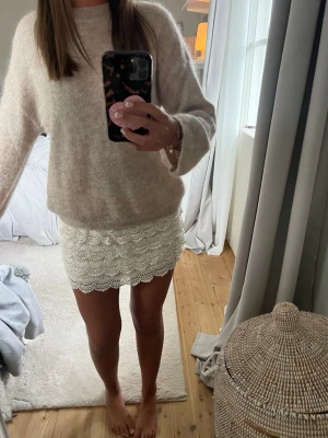 Vit spetskjol med volangkant - Supersöt vit kjol i spets med volangkant och kort passform. Kjolen har ett detaljerat spetsmönster och ger en romantisk vibe. Perfekt att styla med en stickad tröja eller crop top för en trendig look.
